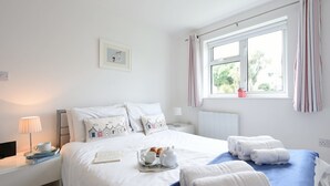 Un lit bien fait, avec du linge de lit blanc et des oreillers, un plateau avec des croissants, une théière et une tasse posés sur la table de chevet.