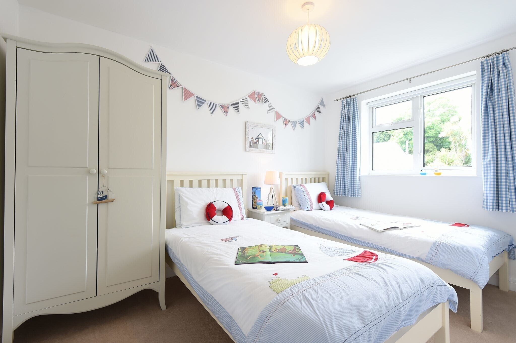 A bedroom with two single beds, a wardrobe, a bedside table with a lamp, and a window with curtains.