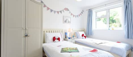 Un dormitorio con dos camas individuales, un armario, una mesita de noche con lámpara y una ventana con cortinas.