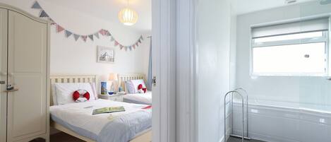 A bedroom with two beds, a wardrobe, a bedside table with a lamp, a window, and a shower area.