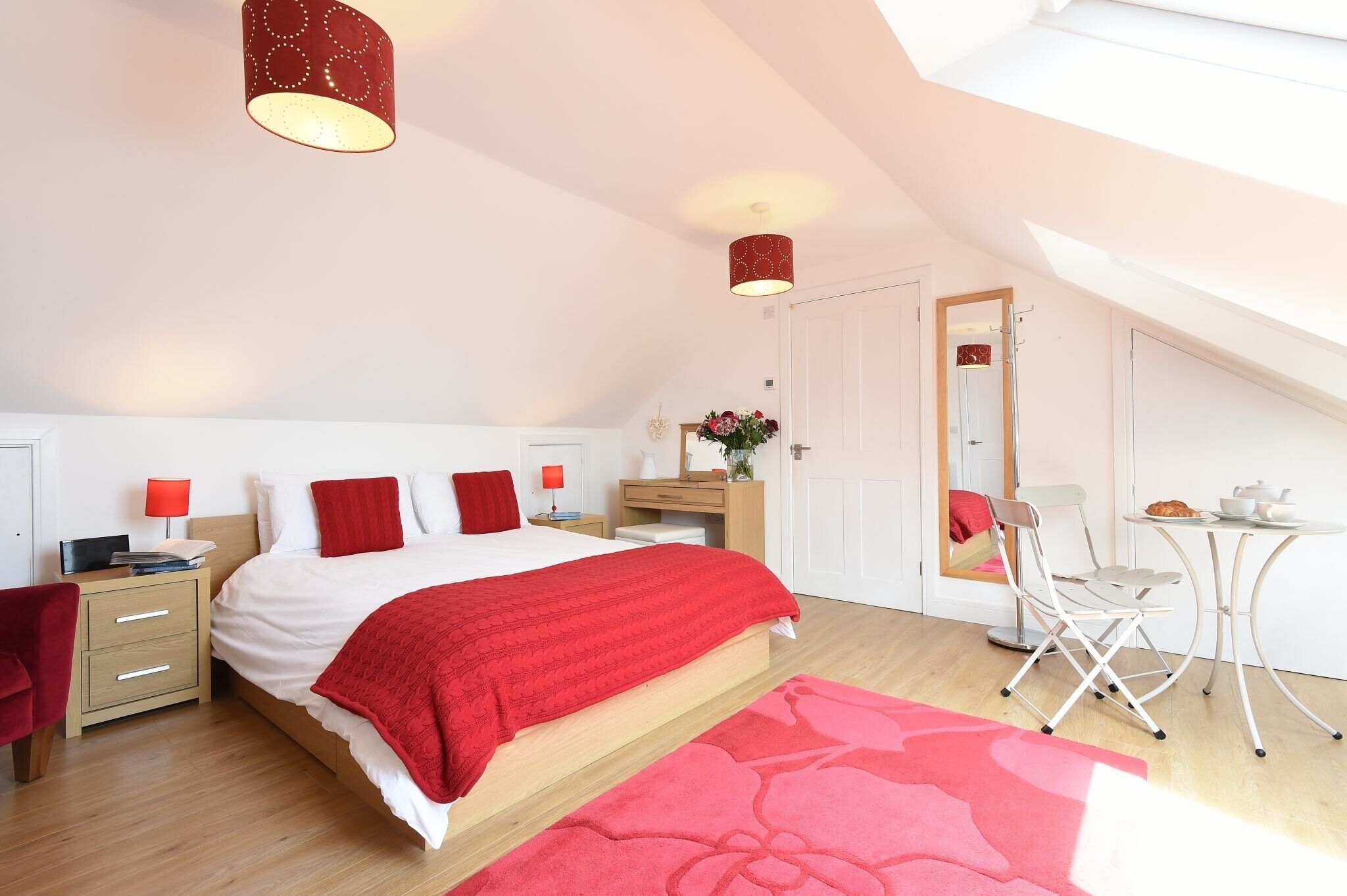 A bedroom with a bed, nightstands, a desk, a chair, and a mirror.