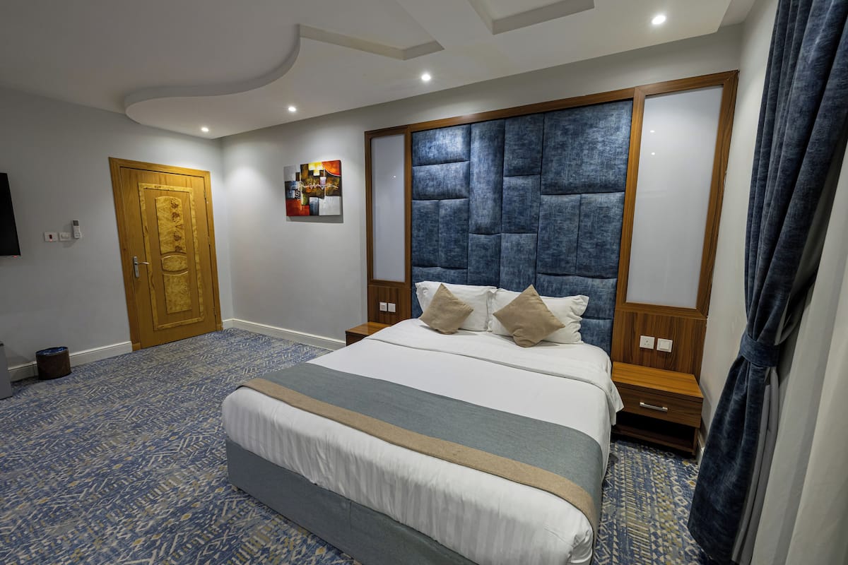 Ein modernes Hotelzimmer mit einem großen Bett, einer Holztür, einem Flachbildfernseher und einem dekorativen Wandbild.