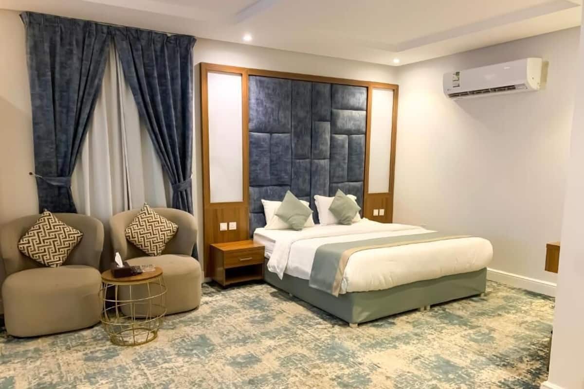 Ein Schlafzimmer mit einem großen Bett, zwei Nachttischen, einem kleinen runden Tisch und einer Couch mit gemusterten Kissen.