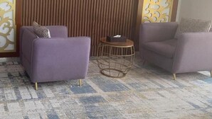 Quarto com duas poltronas roxas, uma mesa redonda pequena e uma parede decorativa com linhas verticais e painéis estampados.