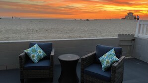 Ein Balkon mit Korbstühlen und einem kleinen runden Tisch, mit Blick auf einen Strand bei Sonnenuntergang.