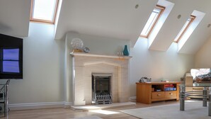 Un salón amplio con chimenea, piso de madera y tragaluces.
