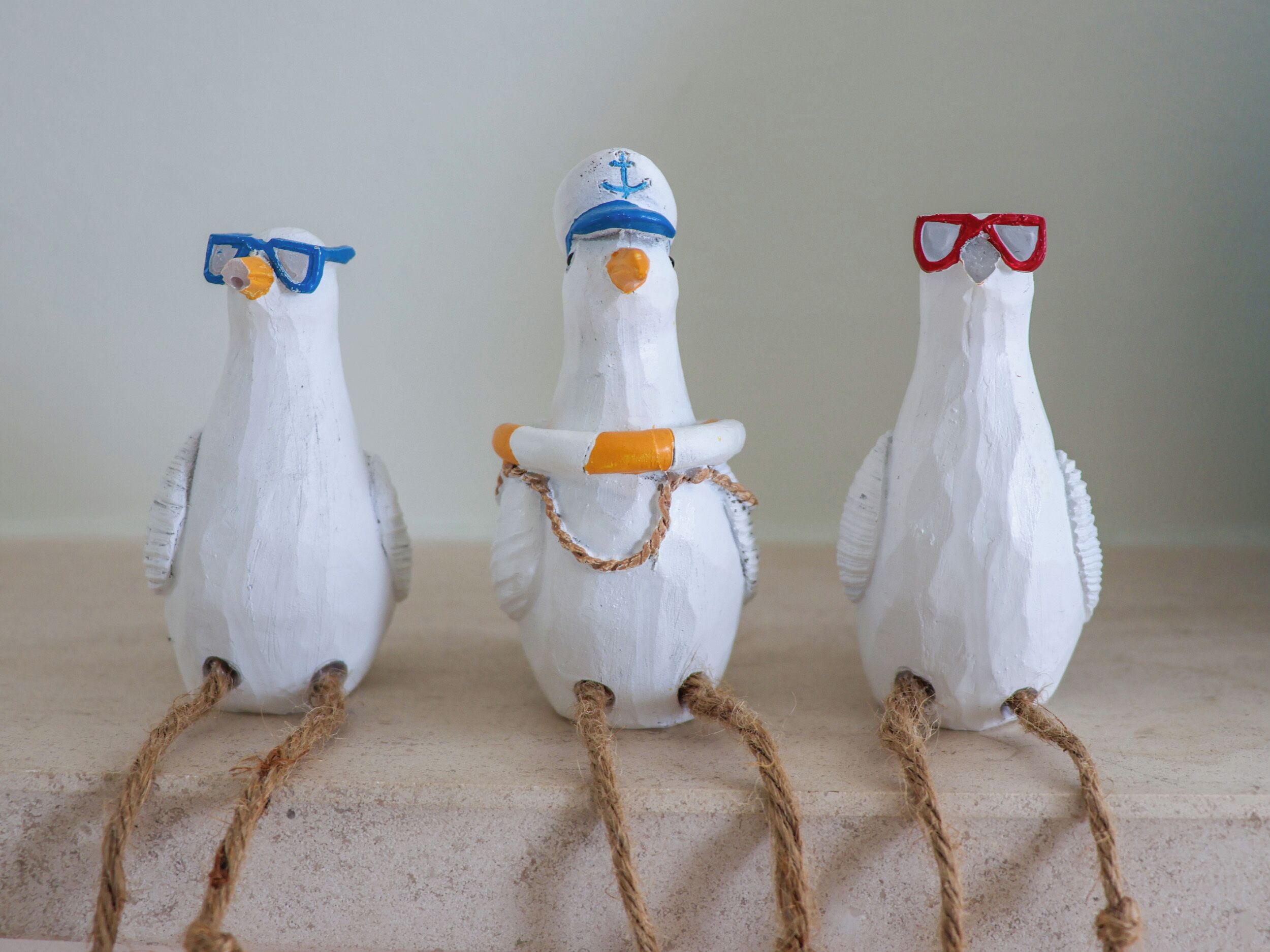 Three white bird figurines with ropes tied around their legs, each wearing different colored glasses.
