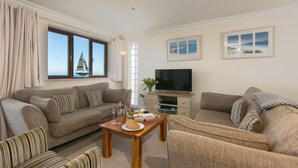 A living room with a sofa, armchairs, a wooden coffee table, a television, and a window with curtains. - Cornerways (St Ives)
