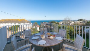 A round wooden table set for dining with chairs, a view of the sea, and a white fence. - Cornerways (St Ives)