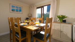 A dining area with a wooden table set for breakfast, chairs, a cabinet, and a view of the outside. - Cornerways (St Ives)
