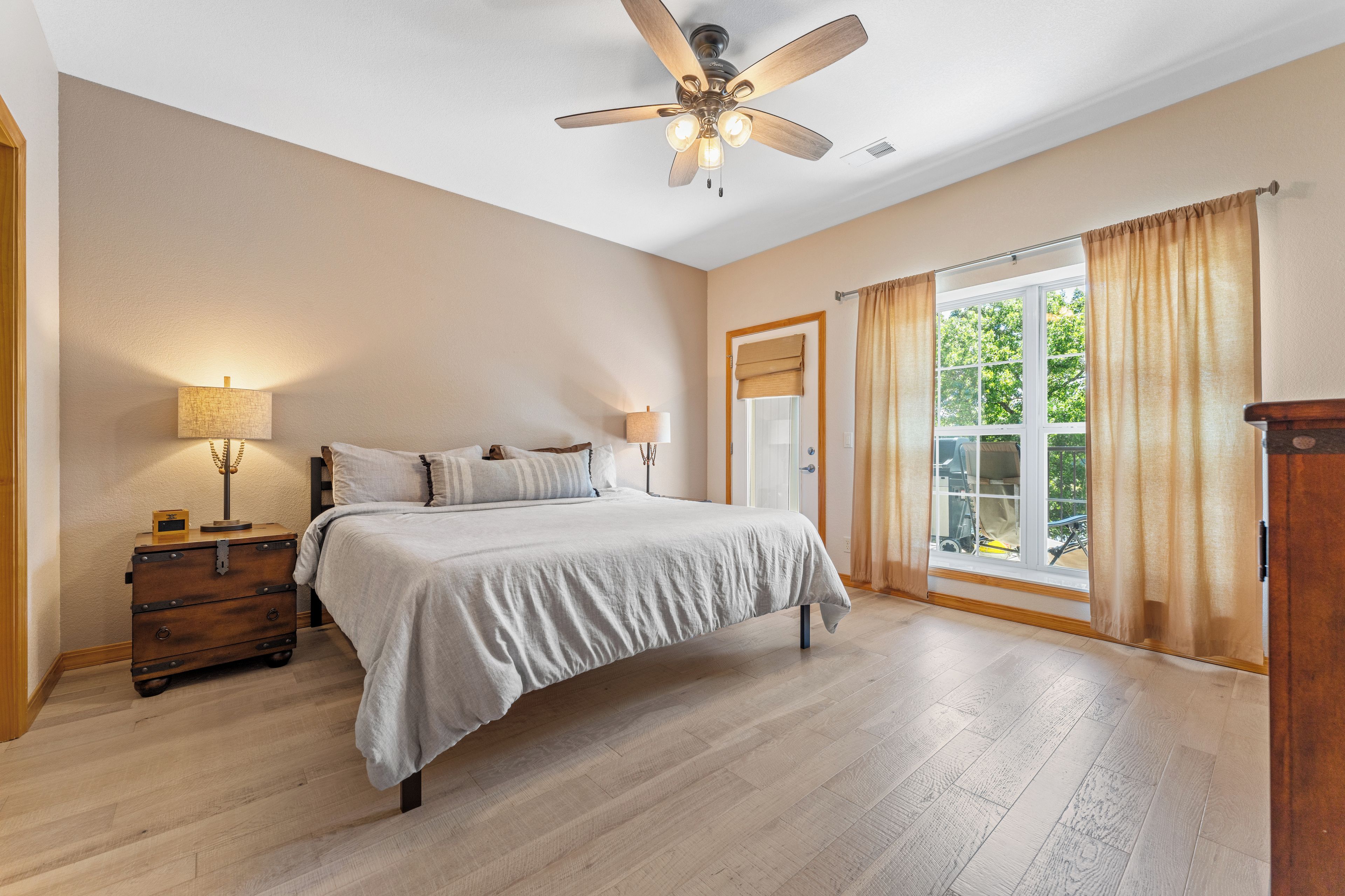 A bedroom with a bed, a ceiling fan, a nightstand, a lamp, and a window with curtains.