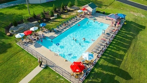 Ein rechteckiger Swimmingpool, umgeben von Liegestühlen und Sonnenschirmen, mit einer Flagge und einem kleinen Gebäude im Hintergrund.