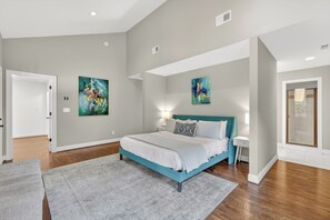 A bedroom with a bed, a nightstand, a wall-mounted light, and two abstract paintings.
