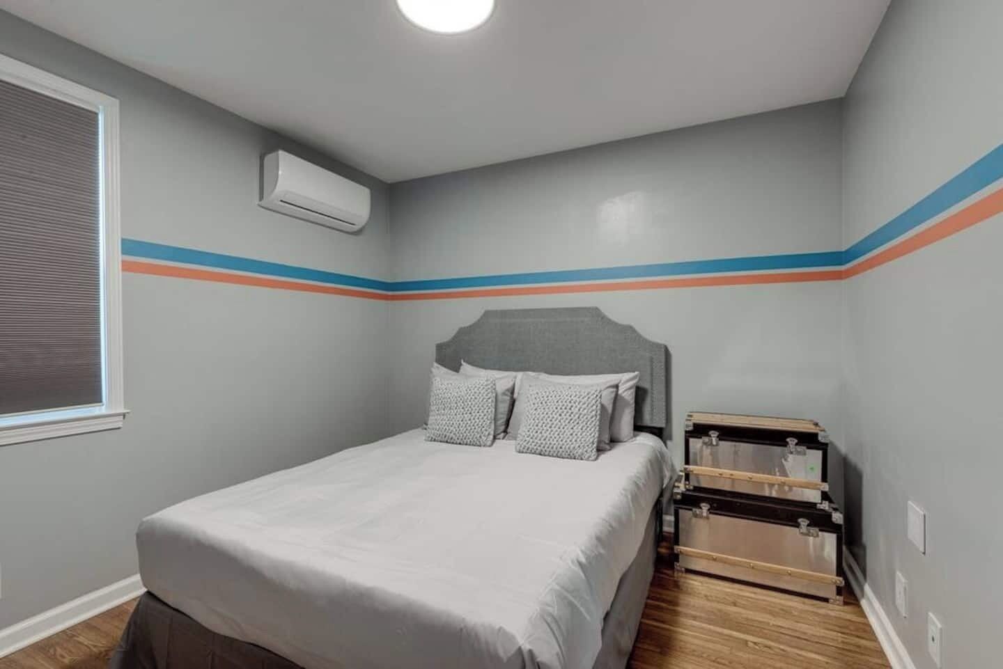 Une chambre à coucher avec un lit, une fenêtre avec des stores, un climatiseur et une commode en bois.