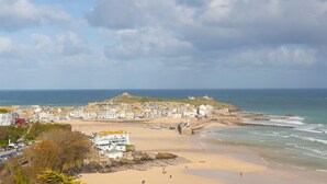 A coastal town with a beach, buildings, and a hill with a fort. - Beach View (St Ives)