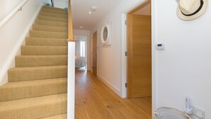A staircase with carpeted steps leading to a room with a wooden floor, a white wall with a framed picture, and a hat hanging on the wall. - Beach View (St Ives)