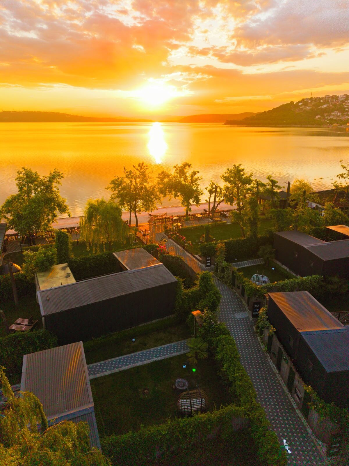 Een resort met een pad dat leidt naar gebouwen, een waterpartij en een zonsondergang.