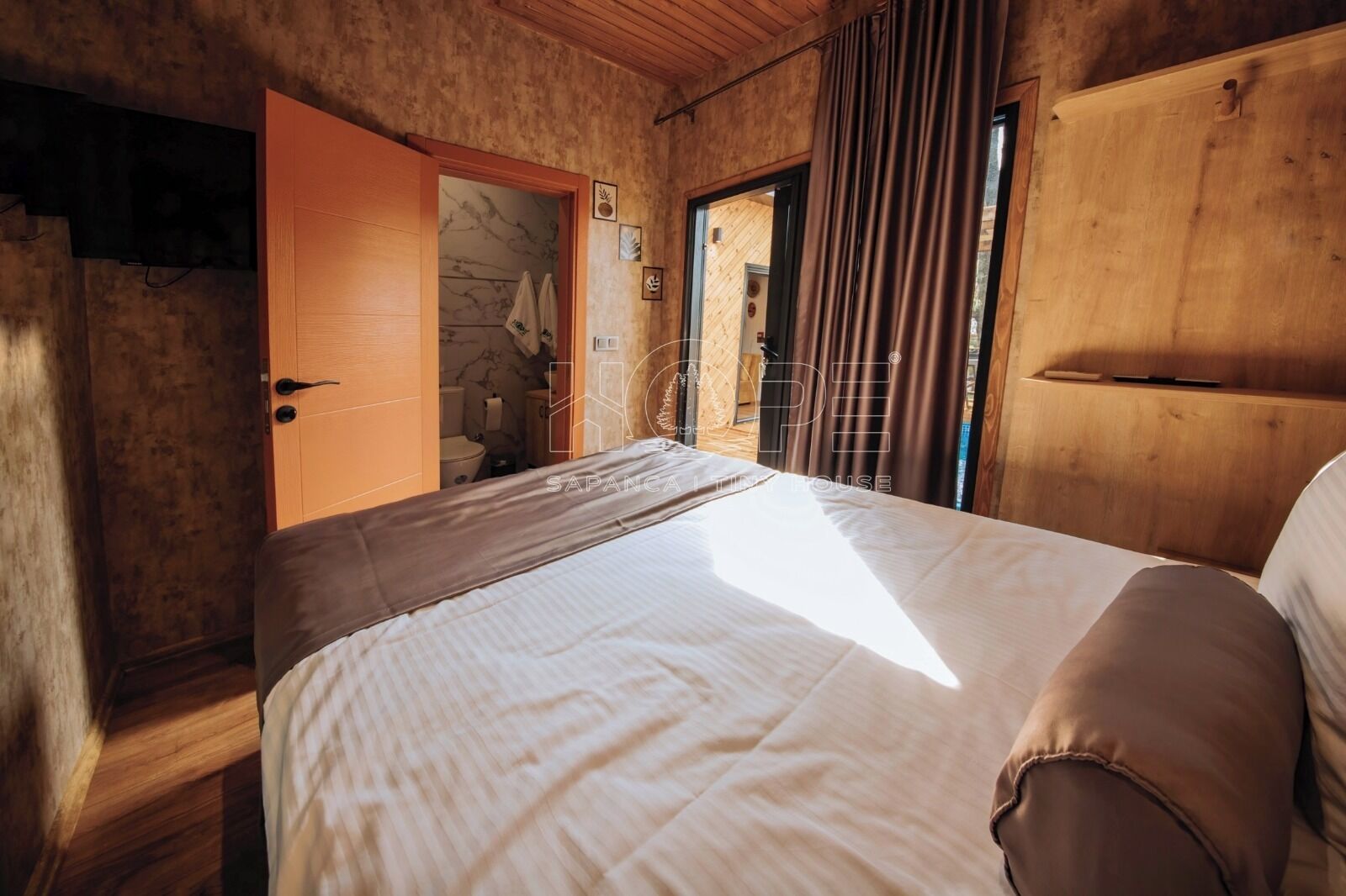 A bedroom with a bed, wooden wardrobe, and a bathroom visible through an open door.