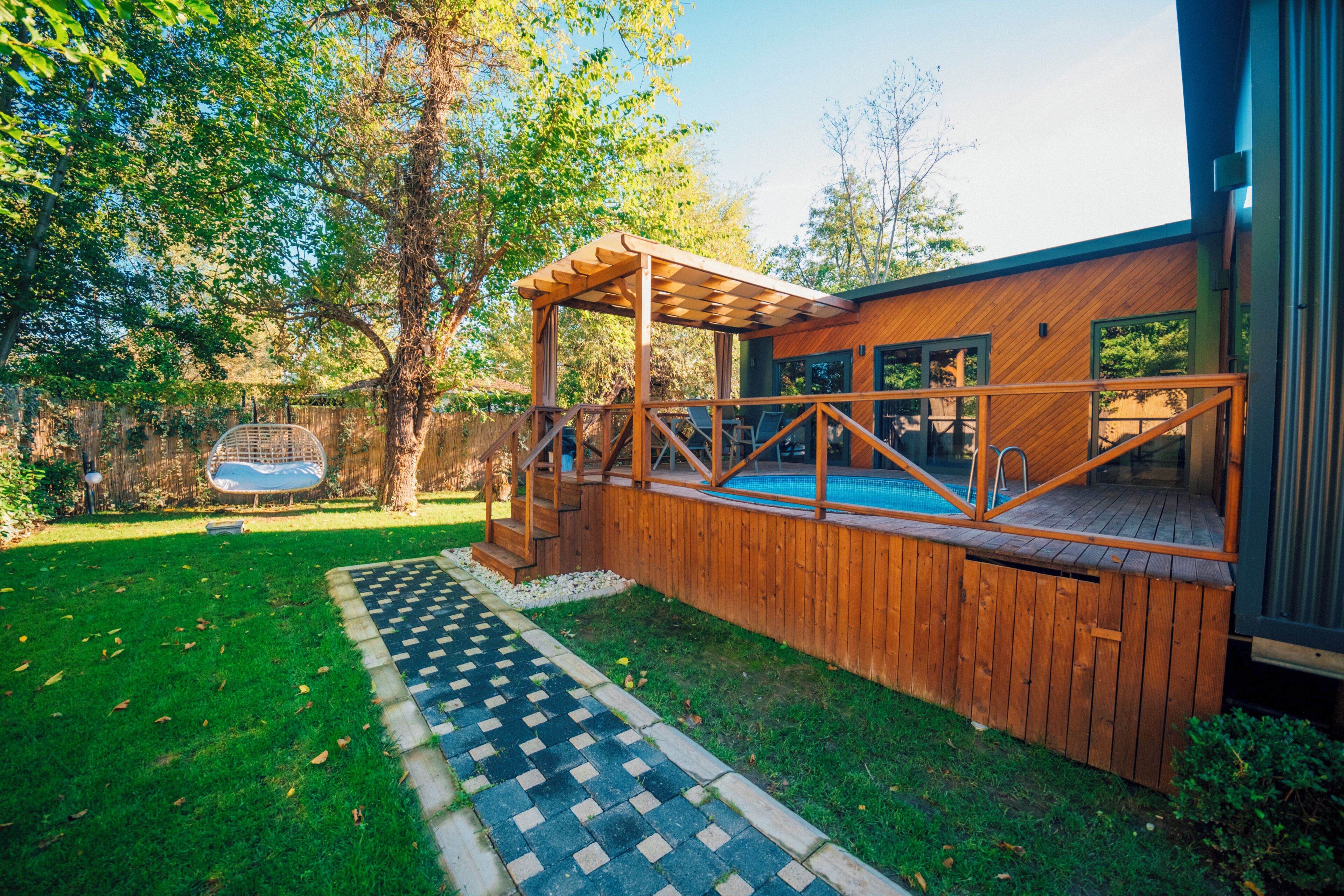 A wooden deck with a pool, surrounded by a garden with a patterned walkway.