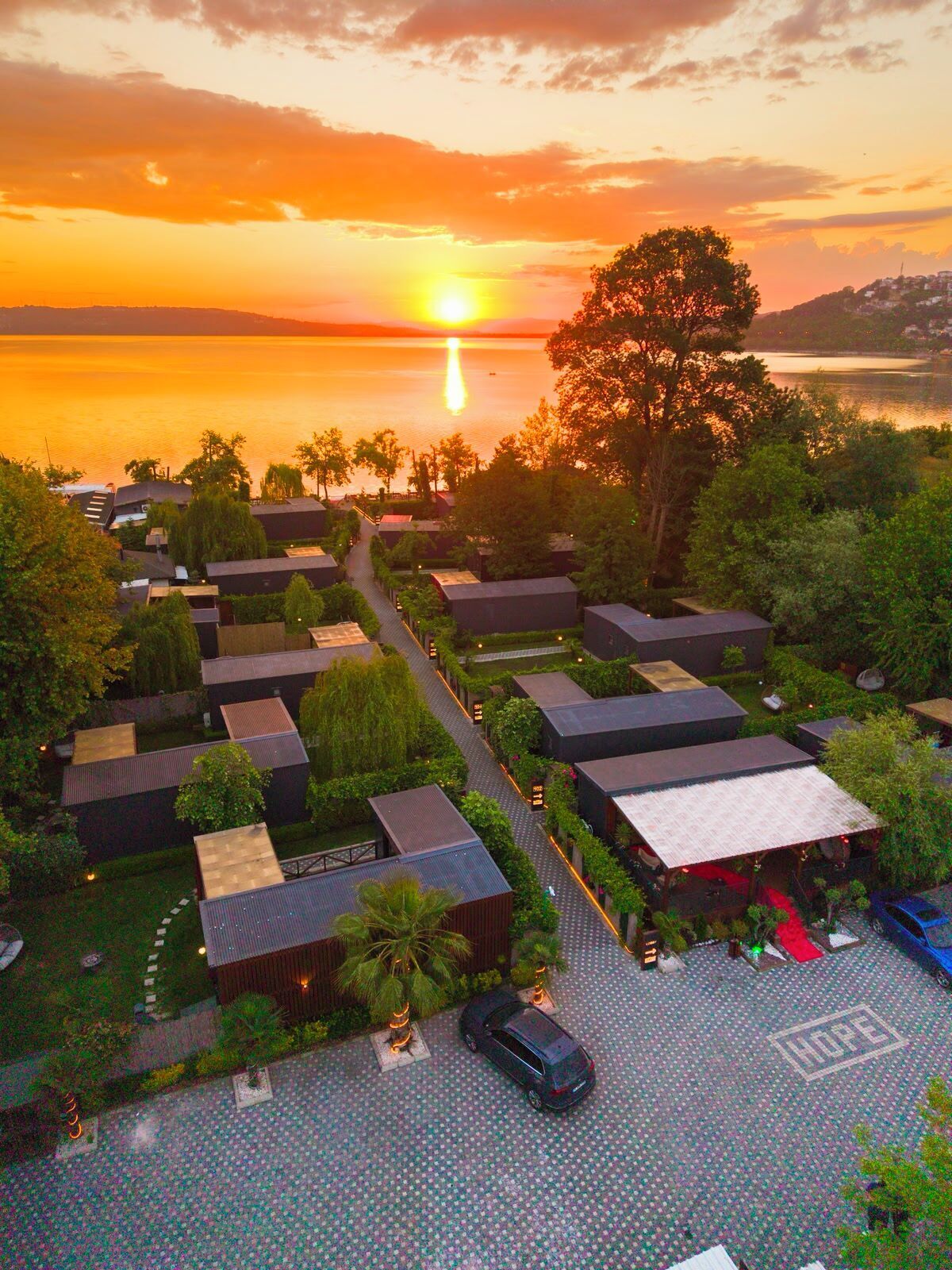 A resort with multiple bungalow-style accommodations, a central pathway, and a view of the sunset over a body of water.