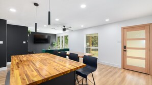 A modern kitchen with a wooden island, black chairs, and a flat-screen TV. - Listen Linda, 5 Bedroom Home Near Bishop Arts (Dallas)