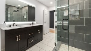 A modern bathroom with a glass-enclosed shower, a large mirror, and a dark-colored vanity. - Listen Linda, 5 Bedroom Home Near Bishop Arts (Dallas)