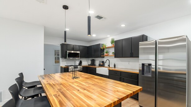 A modern kitchen with a wooden island, black cabinets, stainless steel appliances, and black chairs around the island. - Listen Linda, 5 Bedroom Home Near Bishop Arts (Dallas)