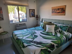 Une chambre  à coucher avec un lit, une fenêtre, une lampe et une affiche accrochée au mur.