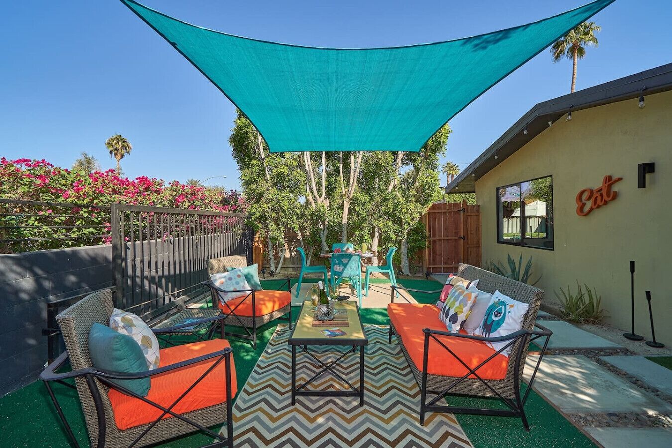 An outdoor patio with wicker furniture, a table, and a teal shade sail.