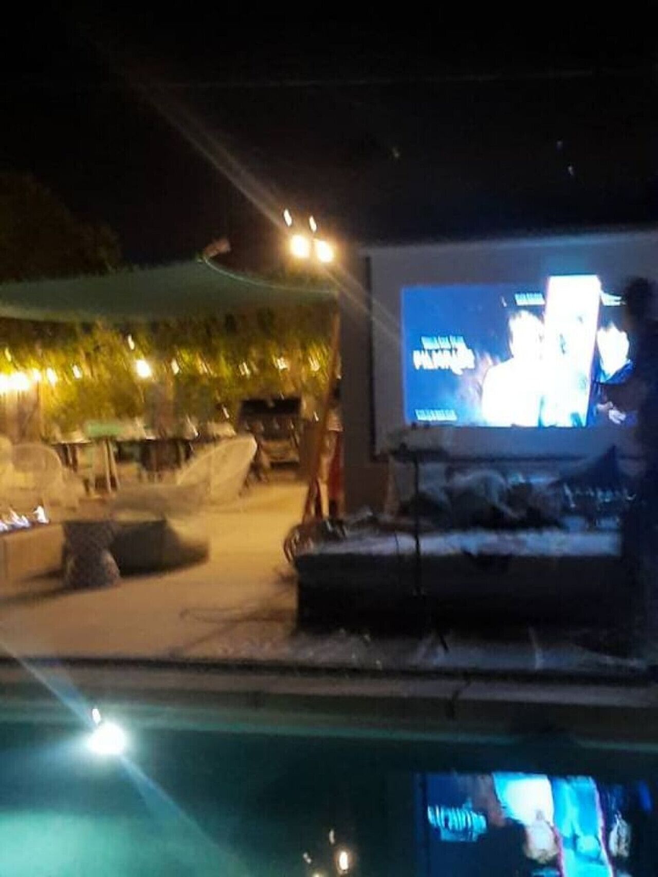 A poolside area with a large screen displaying a movie, outdoor seating, and a lounge chair.