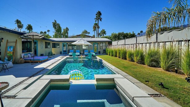A rectangular swimming pool with a floating ball, surrounded by a patio area with chairs and a lounge.