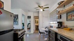 A compact kitchen with a gas stove, oven, and modern appliances. There is a dining area with a table and chairs, and a ceiling fan.