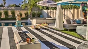 A pool area with a checkered floor, lounge chairs, a table with a board game, and a covered seating area.