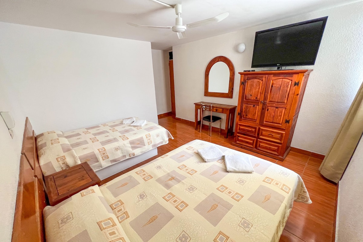 A room with two beds, a desk, a chair, a wardrobe, and a TV.