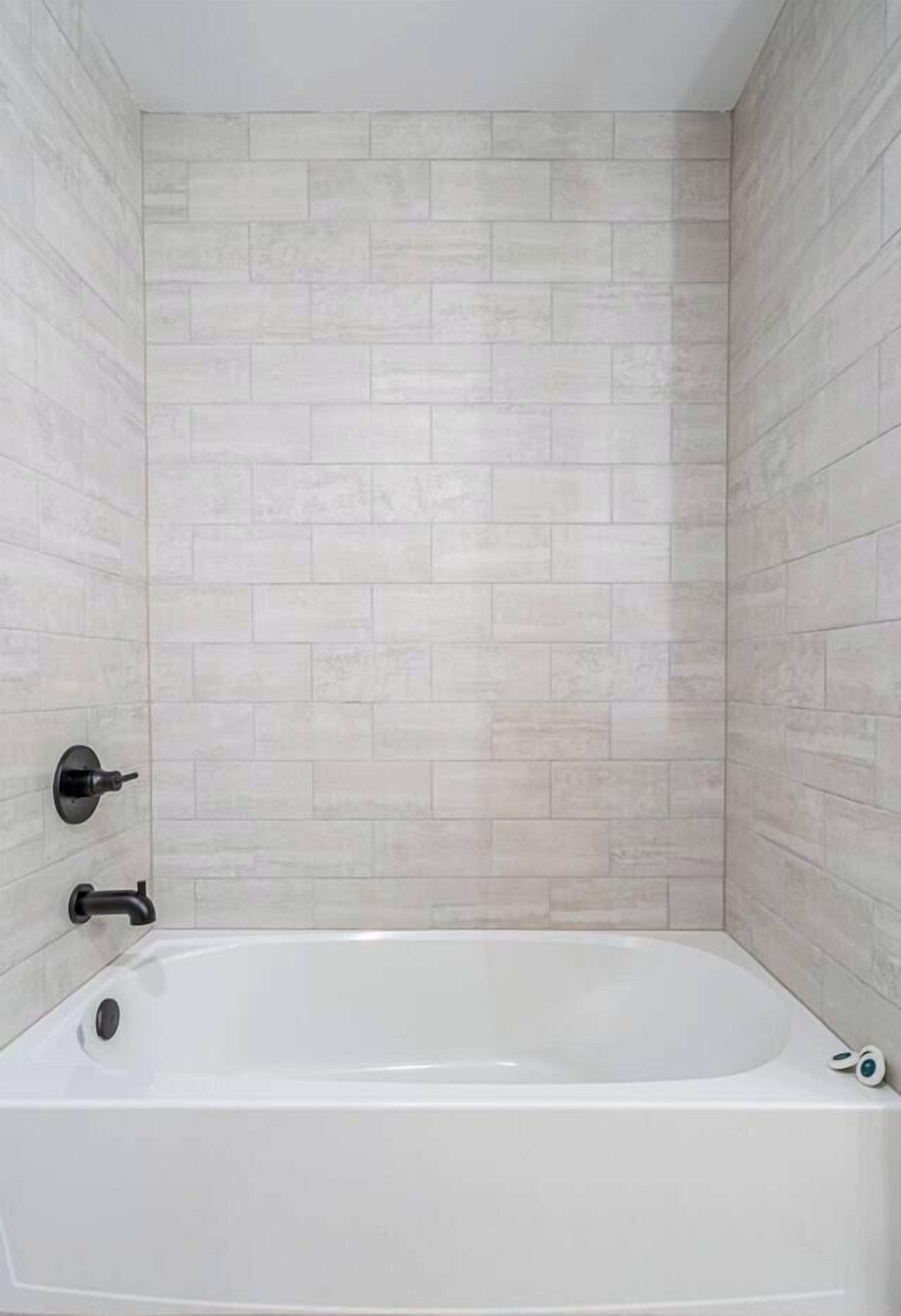Une salle de bain moderne avec une baignoire sur pieds, des murs recouverts de carreaux de couleur claire et un robinet de douche visible.