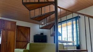 Ein großzügiger Wohnbereich mit einer Wendeltreppe aus Holz, einem grünen Sofa, einem Holzesstisch und einem Fernseher.