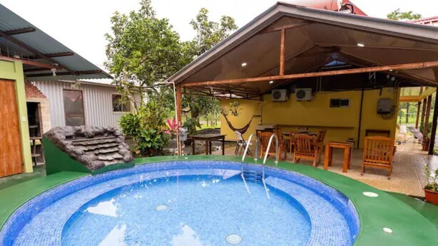 Ein kreisförmiger Pool mit Fliesenrand, umgeben von einer überdachten Terrasse mit Holzmöbeln.