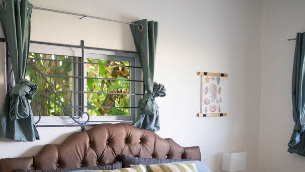 Una cama bien hecha con un cojín a rayas, una toalla enrollada y un cabecero decorativo.