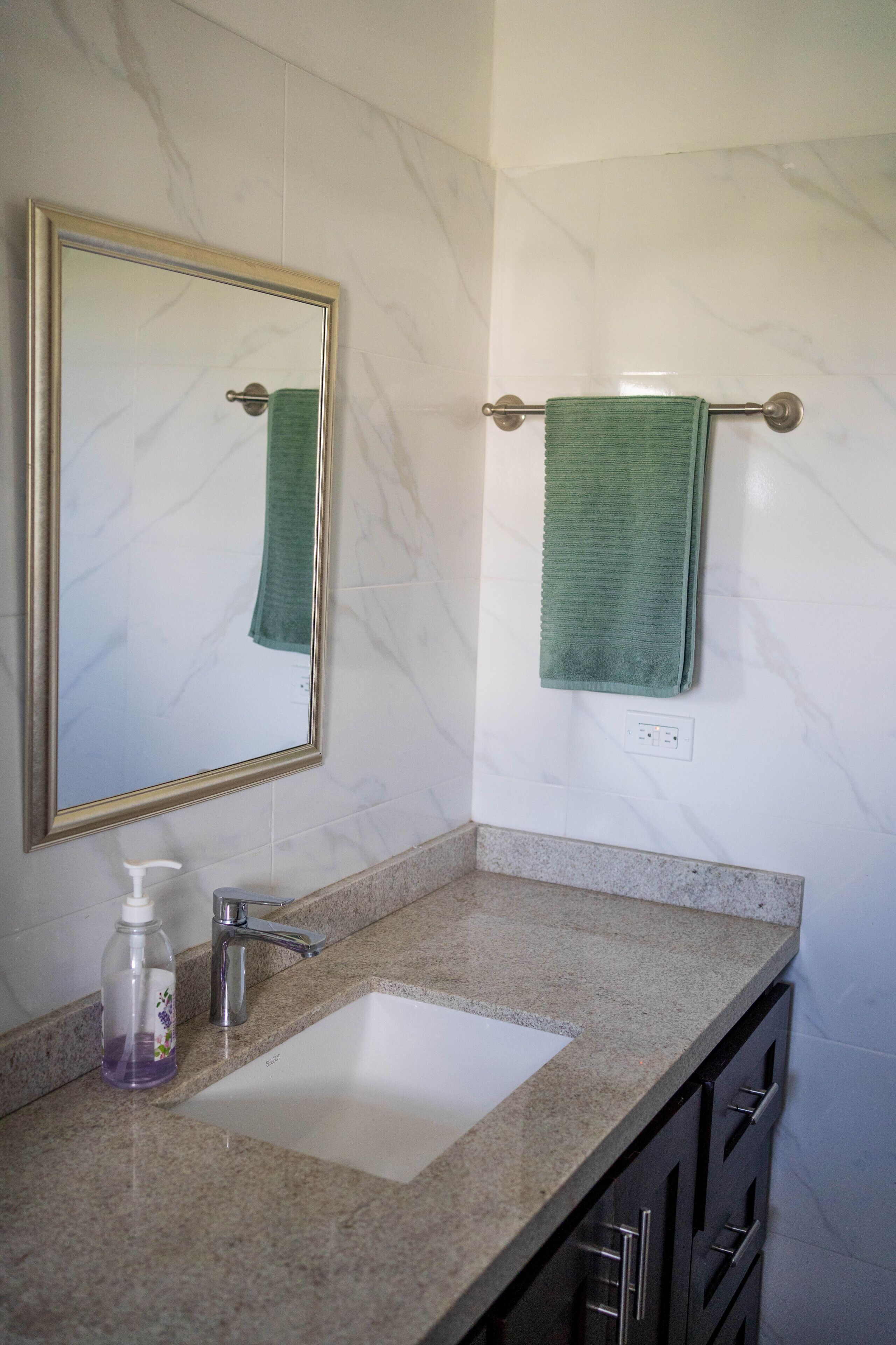 Une salle de bain avec un mur en marbre, un lavabo avec un distributeur de savon et un porte-serviettes sur lequel est posée une serviette verte.