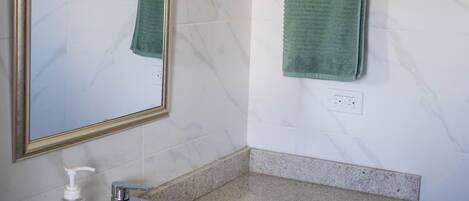 Une salle de bain avec un mur en marbre, un lavabo avec un distributeur de savon et un porte-serviettes sur lequel est posée une serviette verte.