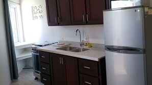Una cocina con armarios de madera oscura, un refrigerador de acero inoxidable, un lavamanos y una ventana con cortina.
