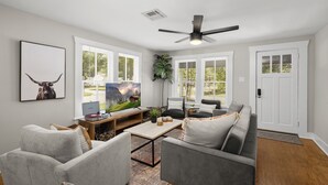 Un salon avec un canapé gris, une table basse, un téléviseur et un ventilateur de plafond.