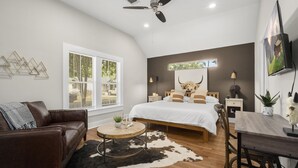 Une chambre avec un lit, un bureau, une chaise, un canapé, un ventilateur de plafond, une fenêtre et un téléviseur fixé au mur.