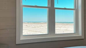 Une chambre dotée d’une grande fenêtre donnant sur une plage et une jetée.