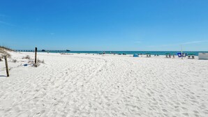 Une vaste plage de sable fin, un ciel bleu dégagé et une jetée qui se profile à l’horizon.