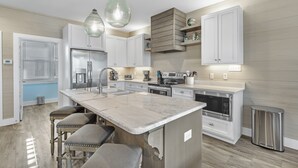 Une cuisine moderne dotée d’un îlot central, d’appareils électroménagers en acier inoxydable et de luminaires suspendus.