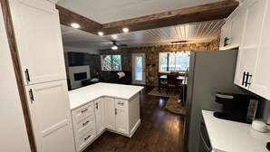 A modern kitchen with white cabinetry, a stone accent wall, and a dining area with a stone fireplace. - The Cottage in the Cove (Denver)