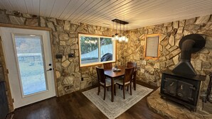 A dining area with a stone wall, wooden ceiling, and a fireplace. - The Cottage in the Cove (Denver)