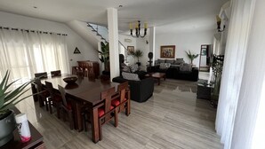 Ein modernes Wohnzimmer mit Essbereich, ausgestattet mit einem Holztisch, schwarzen Sofas und einer Treppe zu einer weiteren Ebene.