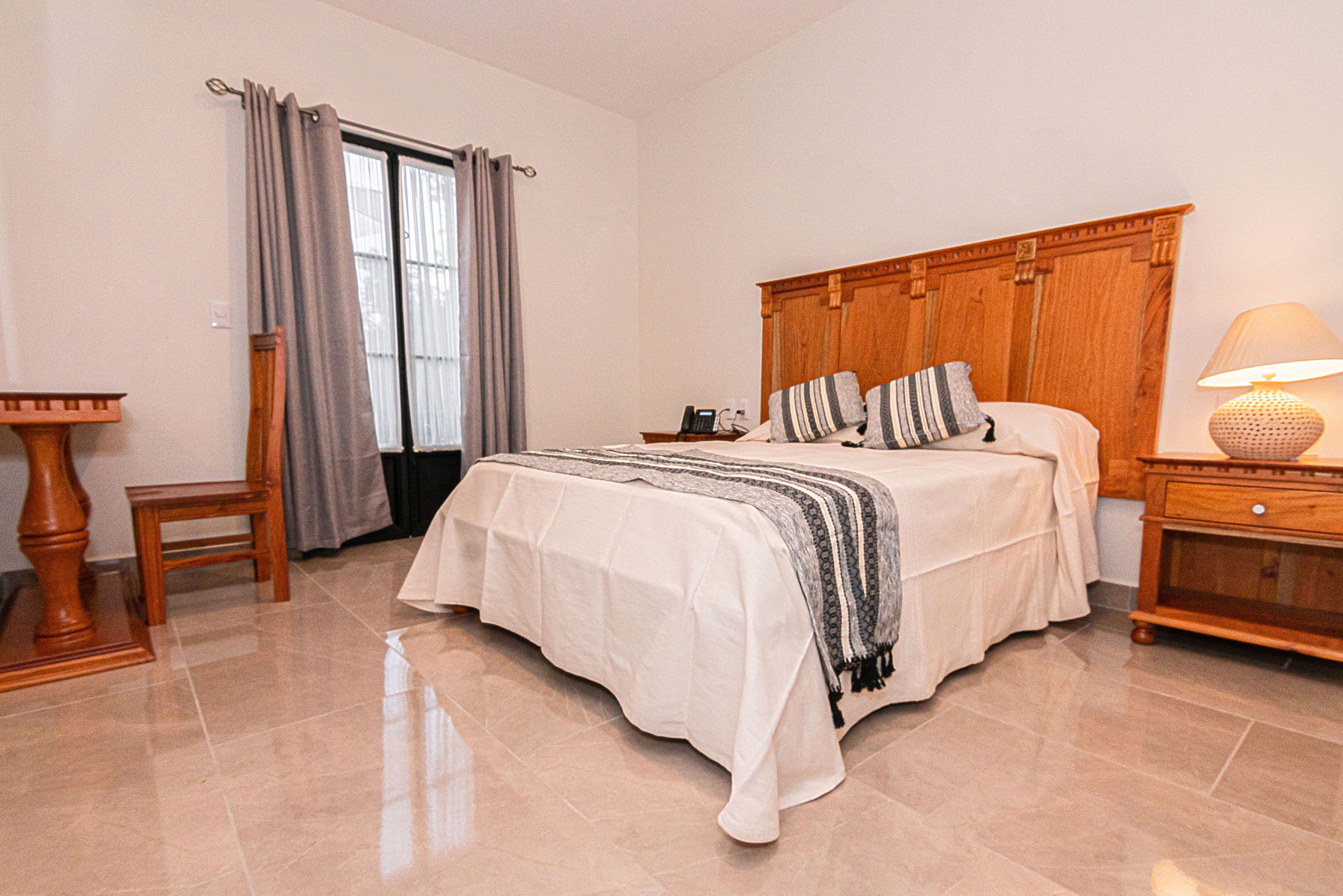 Un dormitorio con cama, mesita de noche, lámpara, silla y ventana con cortinas.